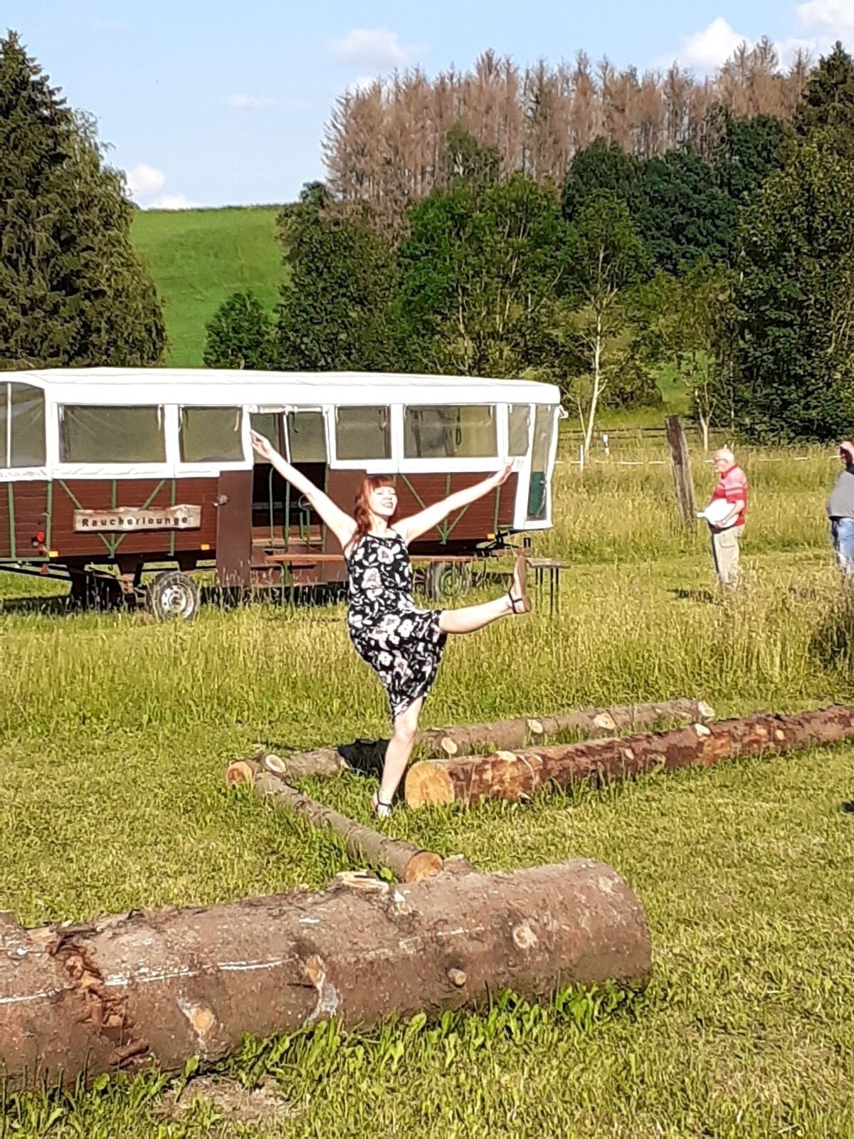 A person standing in a grassy field with a vintage camper van labeled "Raucherlounge" in the background.