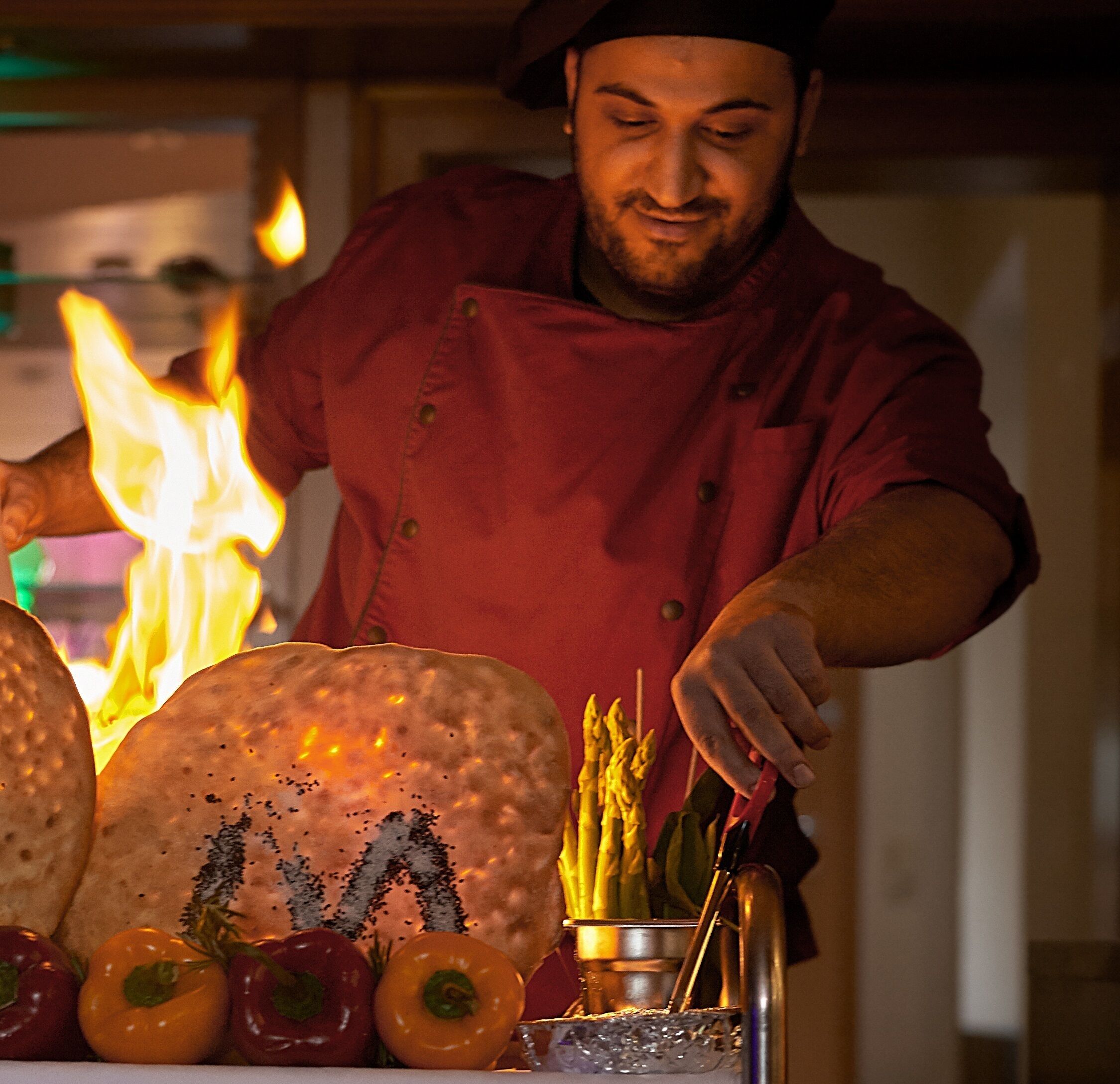 A chef in a red uniform preparing food with vegetables and a large bread roll on a table.