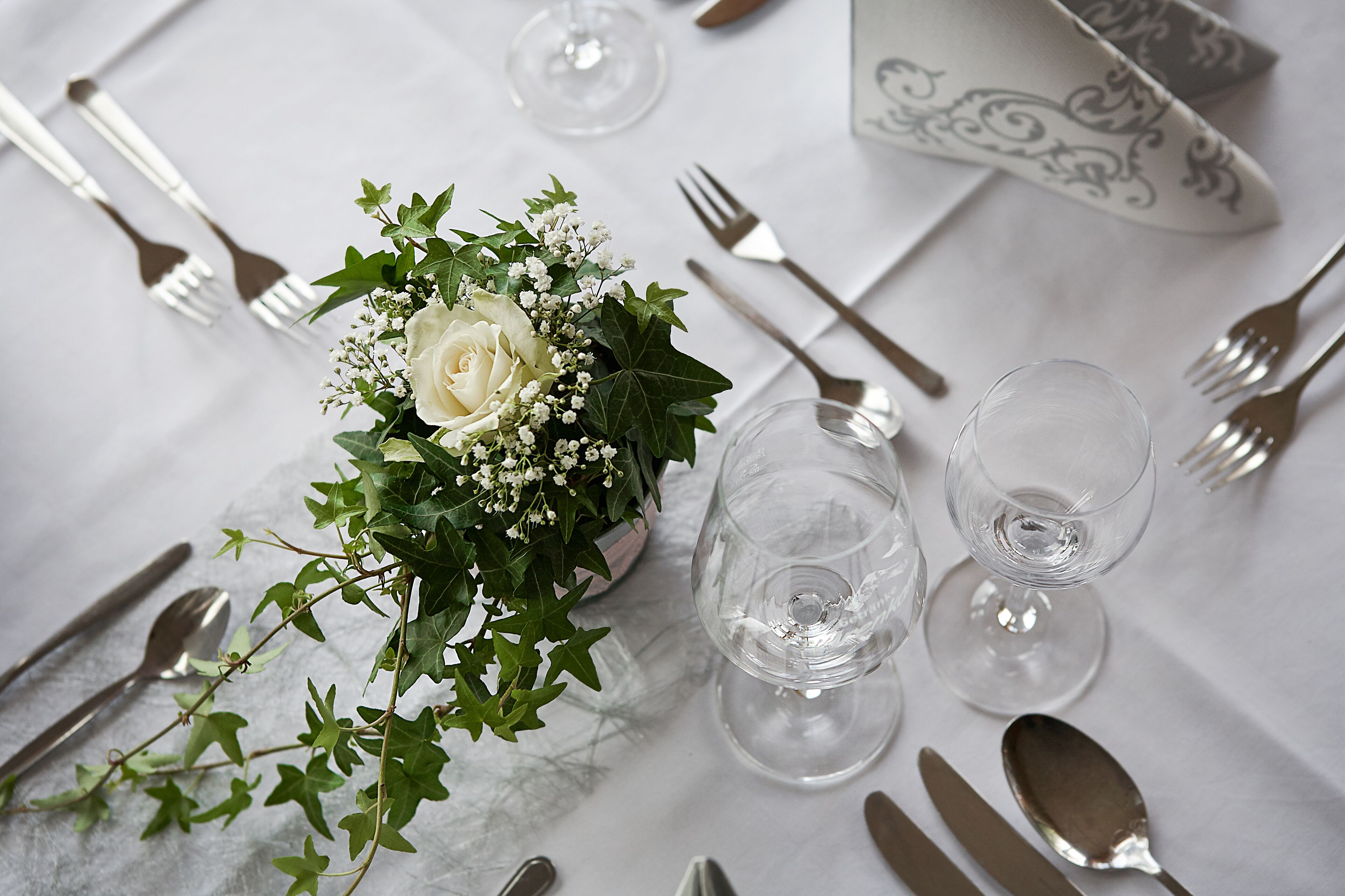 Une table dressée avec une nappe blanche, des couverts en argent et un arrangement floral au centre.