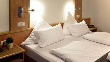 Ein Hotelzimmer mit einem aufgeräumten Bett, einem Nachttisch mit Lampe und einem kleinen Topfpflänzchen.