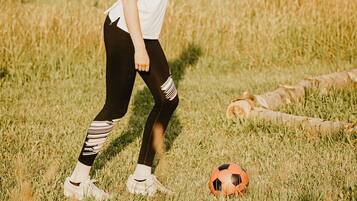 Eine Person spielt Fußball auf einer Wiese, im Hintergrund ist ein Fußballtor zu sehen.
