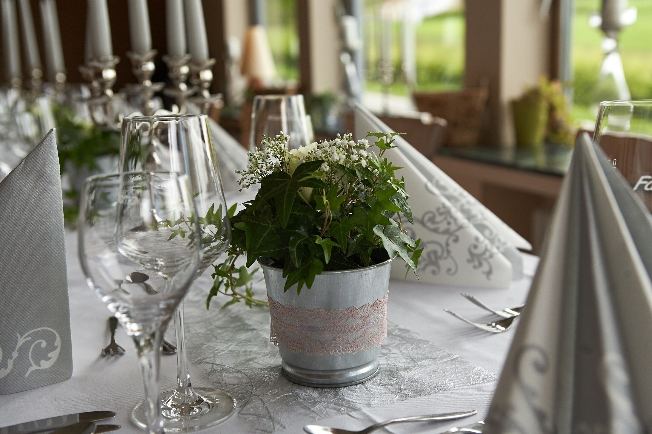 Una mesa dispuesta para un evento formal, con cubertería de cristal, vajilla y un centro de mesa con flores.