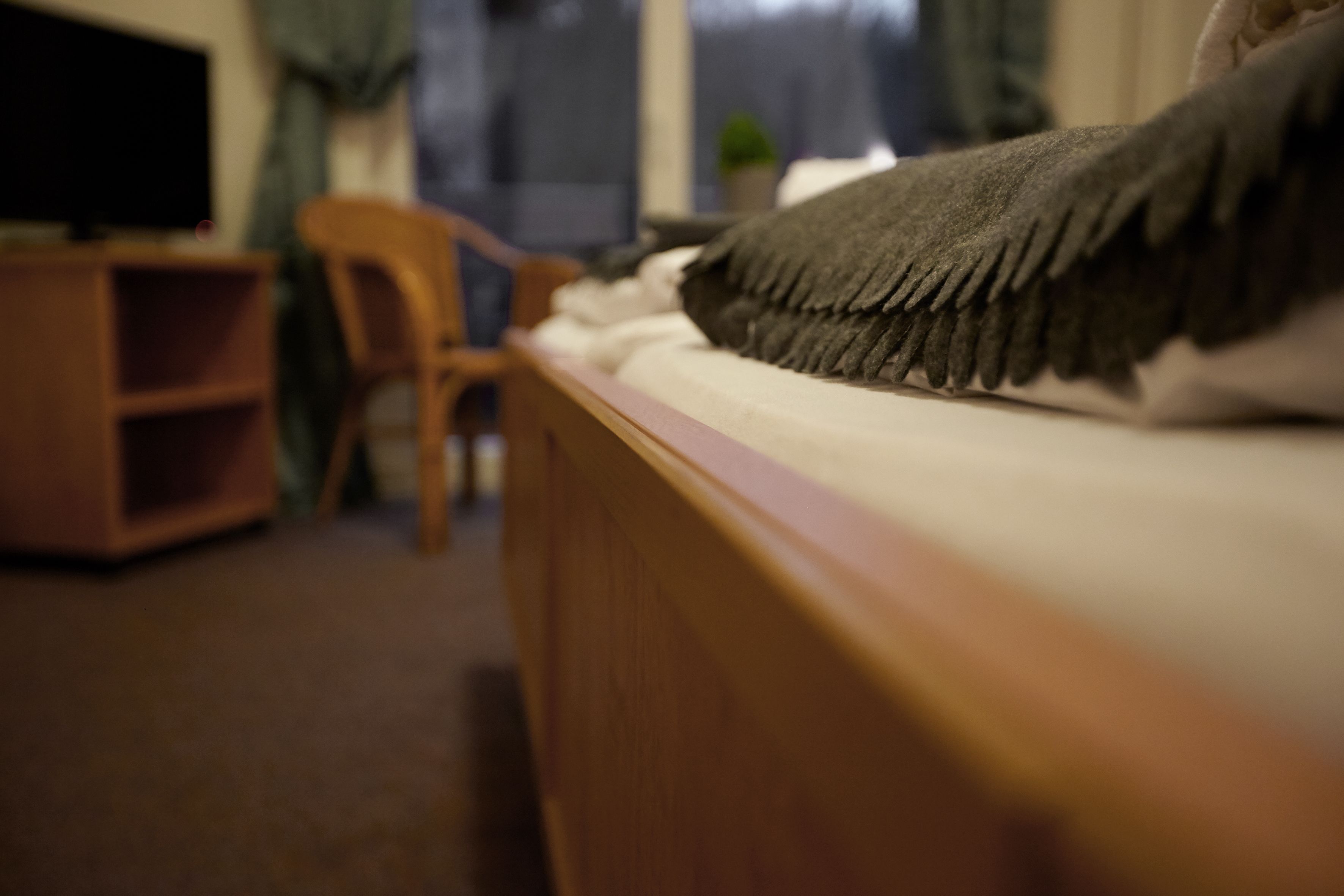 A bedroom with a wooden headboard, a bed with a blanket, a television on a wooden stand, and a chair.