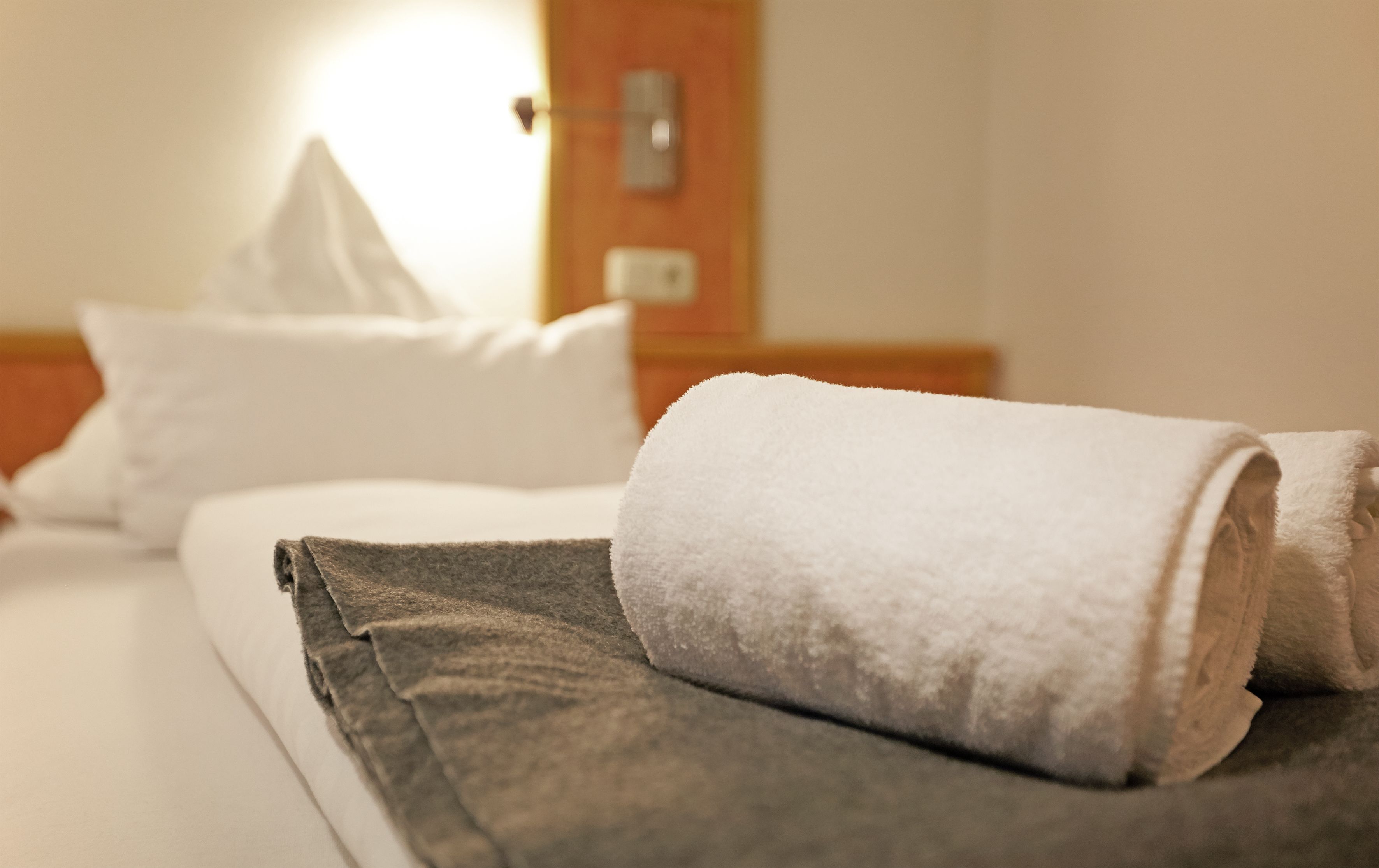 A neatly made bed with a rolled white towel and a folded gray towel.