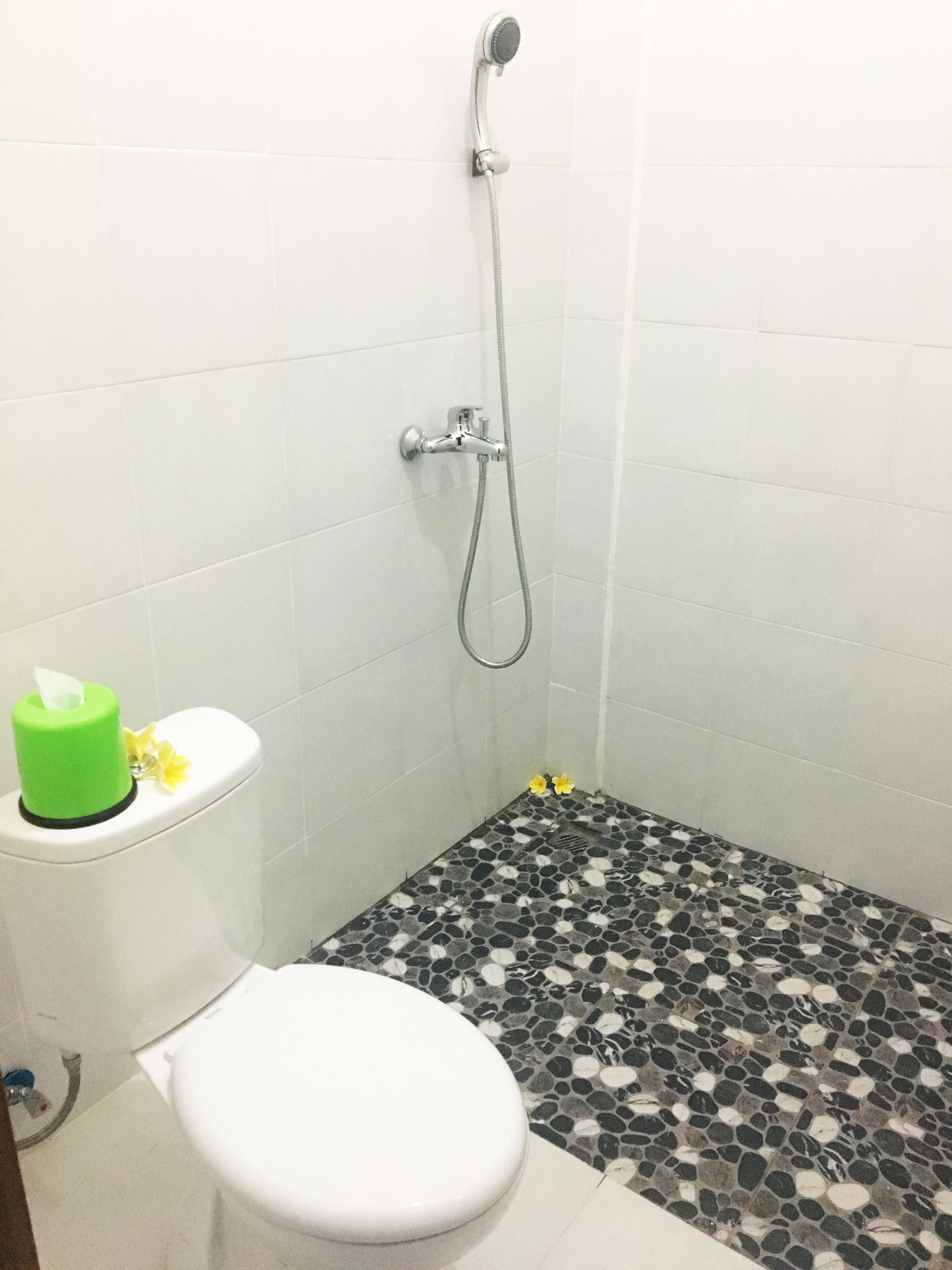 Een badkamer met een wit toilet, een douche met een handdouche en een vloer met een kiezelpatroon.