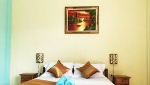 A neatly made bed with two pillows, a blue towel, and a decorative painting above it. - Repag Wayan Canggu Hostel (Canggu)