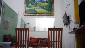 A room with a green wall, a wooden chair, a sofa with patterned cushions, a painting of a landscape, and a mirror. - Repag Wayan Canggu Hostel (Canggu)