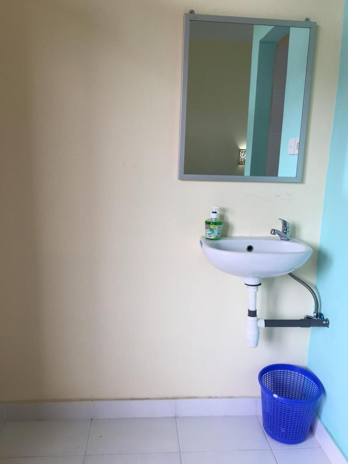 Um banheiro com pia branca, espelho e cesto de plástico azul.