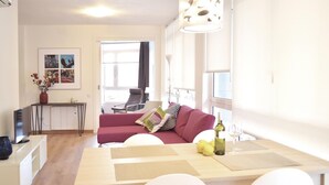 Een moderne woonkamer met een rode bank, een eettafel met stoelen, een televisie en een bloemenvaas.