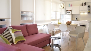 Een moderne woonkamer met een roze bank, witte stoelen en een kleine tafel.