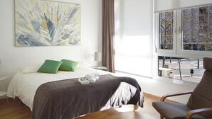 Een moderne hotelkamer met een groot bed, uitzicht op de stad door een groot raam en een abstract kunstwerk aan de muur.