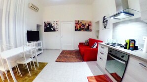 A compact living space with a dining area, a red sofa, a kitchen with a stove, and two paintings on the walls. - Casa G&G Pignasecca 2 in the heart of Naples (Napoli)