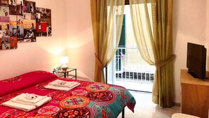 A hotel room with a bed, a wall of pictures, a balcony with a view, and a television on a wooden table. - Casa G&G Pignasecca 2 in the heart of Naples (Napoli)