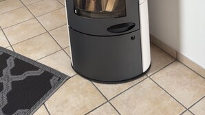 A modern wood-burning stove with a glass door, positioned in a corner of a room with wooden flooring and a tiled floor. - Beautiful apartment in an ideal location for a relaxing, restful vacation (Hausham - Agathried)