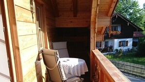 A wooden balcony with a chair and table, a wooden floor, and a view of a house. - Beautiful apartment in an ideal location for a relaxing, restful vacation (Hausham - Agathried)