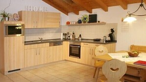 A kitchen with wooden cabinets, a built-in oven, and a dining area with a table and chairs. - Beautiful apartment in an ideal location for a relaxing, restful vacation (Hausham - Agathried)
