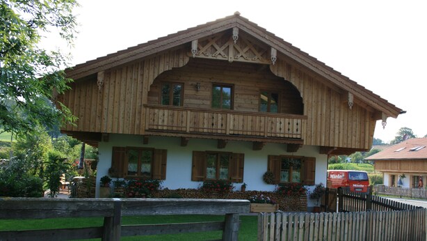A wooden chalet with a balcony, a wooden fence, and a red van parked outside. - Beautiful apartment in an ideal location for a relaxing, restful vacation (Hausham - Agathried)