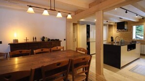 Une table à manger en bois avec des chaises, un coin cuisine doté d’un plan de travail noir et une grande fenêtre.
