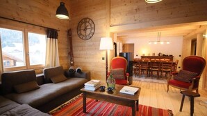 L’intérieur d’un chalet confortable, avec des murs en bois, comprenant un canapé, des fauteuils, une table à manger et une horloge au mur.