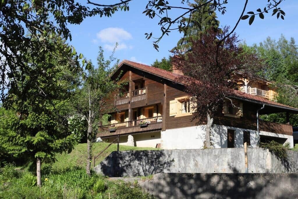 Ein zweigeschossiges Holzhaus mit Balkon, umgeben von Grünpflanzen und Bäumen.