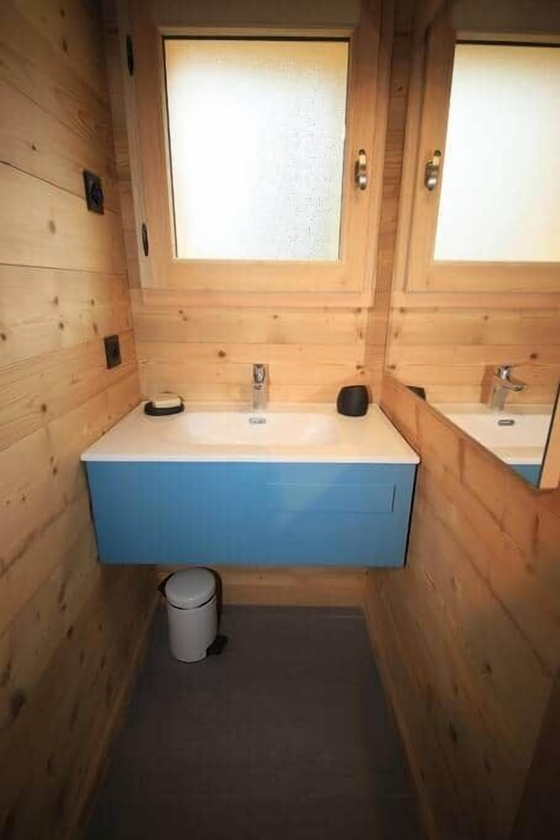 Ein kleines Badezimmer aus Holz mit einem Waschbecken, einem Spiegel und einem Mülleimer.