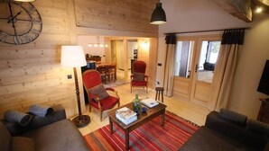 Un salon chaleureux avec un canapé, un fauteuil et une table basse, des murs en bois et une grande fenêtre.