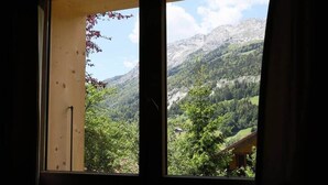 Une fenêtre donnant sur un paysage montagneux, avec des arbres et une maison.