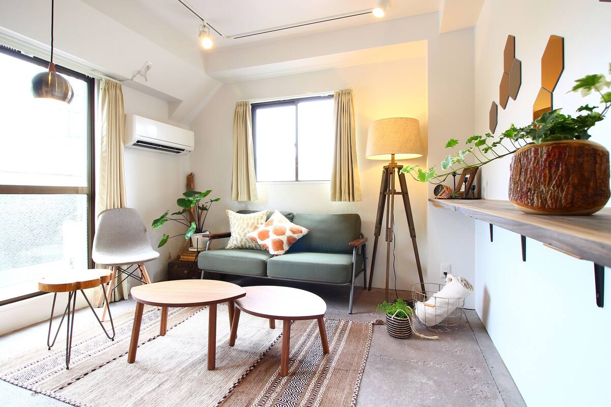 Una sala de estar moderna con un sofá, dos mesas redondas, una lámpara de pie y una planta en maceta.