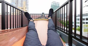 A hammock on a balcony with a cityscape view. - Koru Takanawa Gateway Hostel Cafe&Bar (Tokyo)
