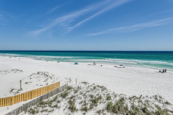 A beach with white sand, a wooden fence, and the ocean.