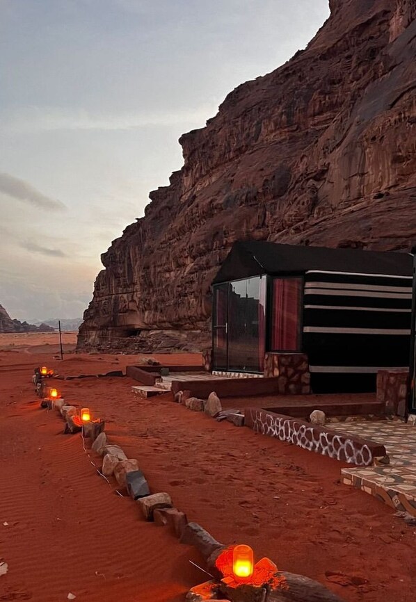 A desert landscape with a building featuring a glass facade and a covered outdoor area. - Wadi Rum Desert Tours Camp (Wadi Rum)