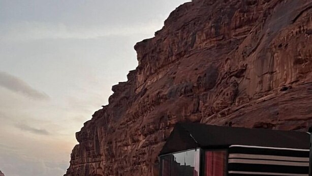 A desert landscape with a rock formation and a small building with a glass facade. - Wadi Rum Desert Tours Camp (Wadi Rum)