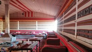 A room with striped patterned walls and a ceiling, featuring a sofa and tables with various items. - Wadi Rum Desert Tours Camp (Wadi Rum)