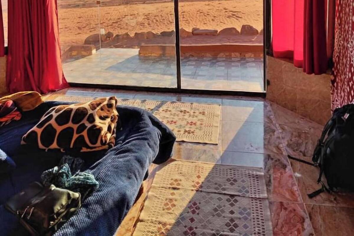 A room with a large window offering a desert view, patterned curtains, a bed with a giraffe-patterned pillow, and a rug.