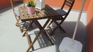 Une table et des chaises en bois sont disposées sur un balcon, accompagnées d’une plante en pot et d’une lanterne blanche.