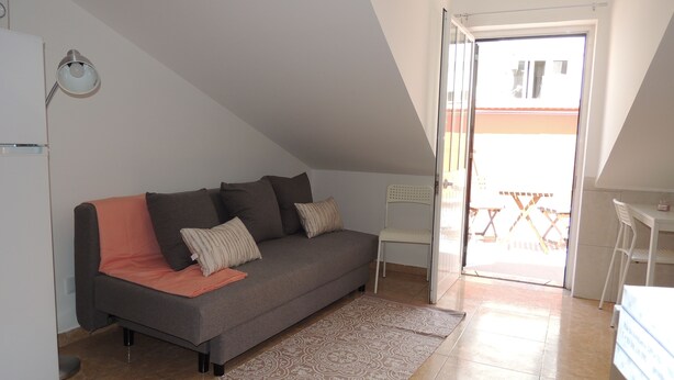 Un petit appartement moderne avec un canapé gris, une chaise blanche, une petite table et une grande fenêtre.