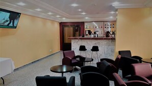 Un espace bar doté d’un comptoir en marbre, de chaises noires et violettes, et d’un téléviseur fixé au mur.