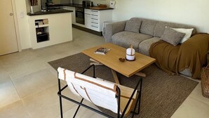Ein kompakter Wohnbereich mit Küchenzeile, einer Couch, einem Esstisch mit Stühlen und einer Pendelleuchte.
