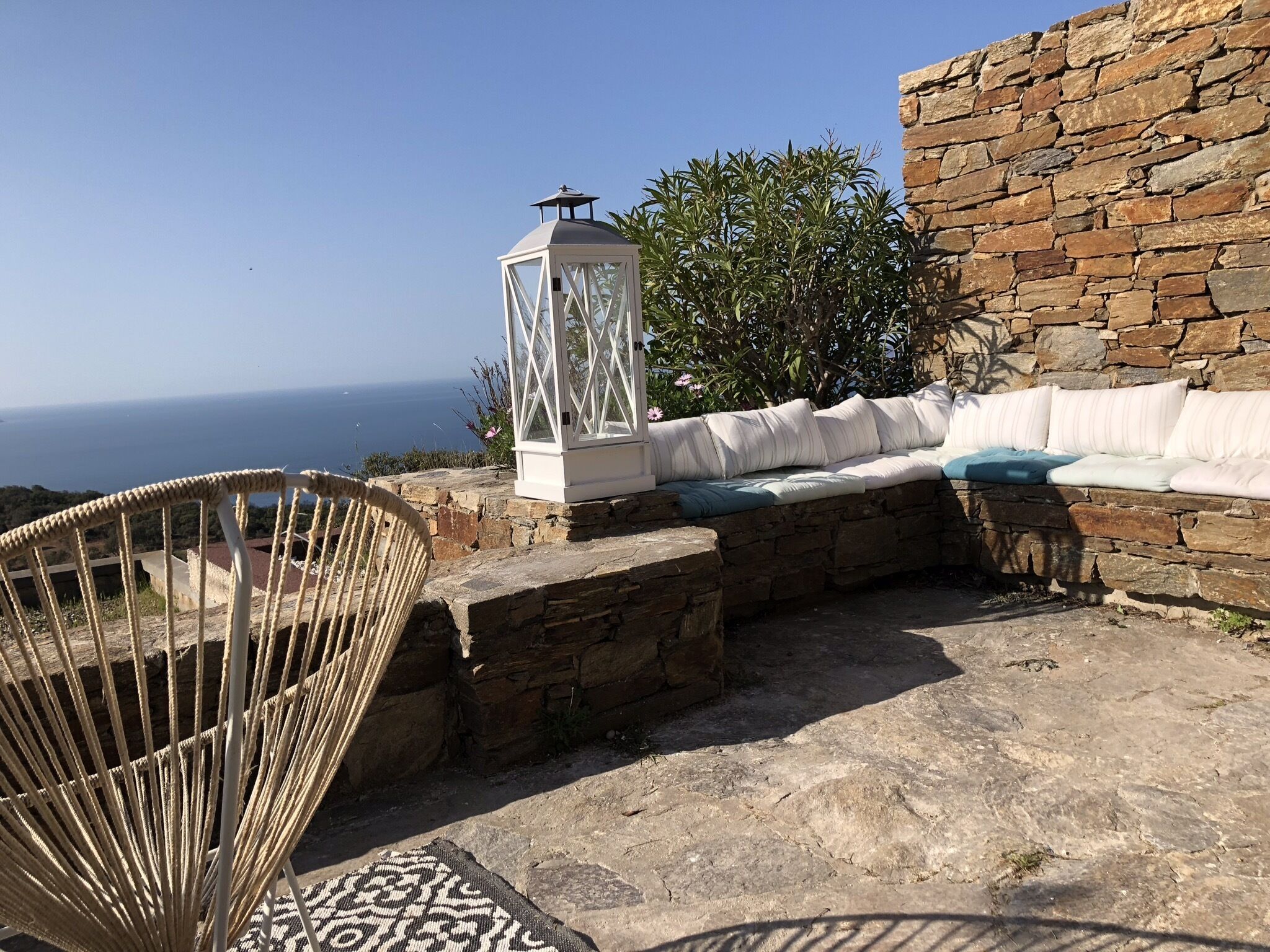 A stone wall, a white lantern, a wicker chair, and a cushioned bench with pillows.