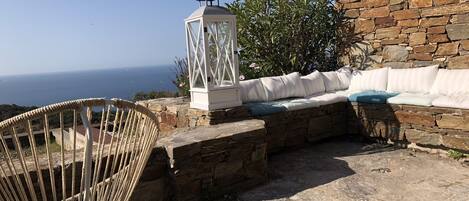 A stone wall, a white lantern, a wicker chair, and a cushioned bench with pillows.