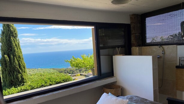 Ein Schlafzimmer mit großem Fenster und Blick auf das Meer und die grüne Landschaft.