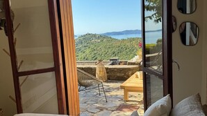 Ein Schlafzimmer mit einem großen Bett, einem Holzsessel und Blick auf eine Hügel- und Wassersicht durch eine Glastür.