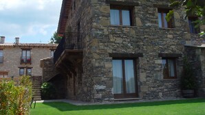 Ein Steinhaus mit Balkon, großen Fenstern und einem gepflegten Rasen.