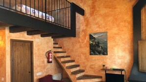Ein gemütliches Wohnzimmer mit einer Holztreppe, einem roten Sofa, einem Kamin und einem Gemälde an der Wand.