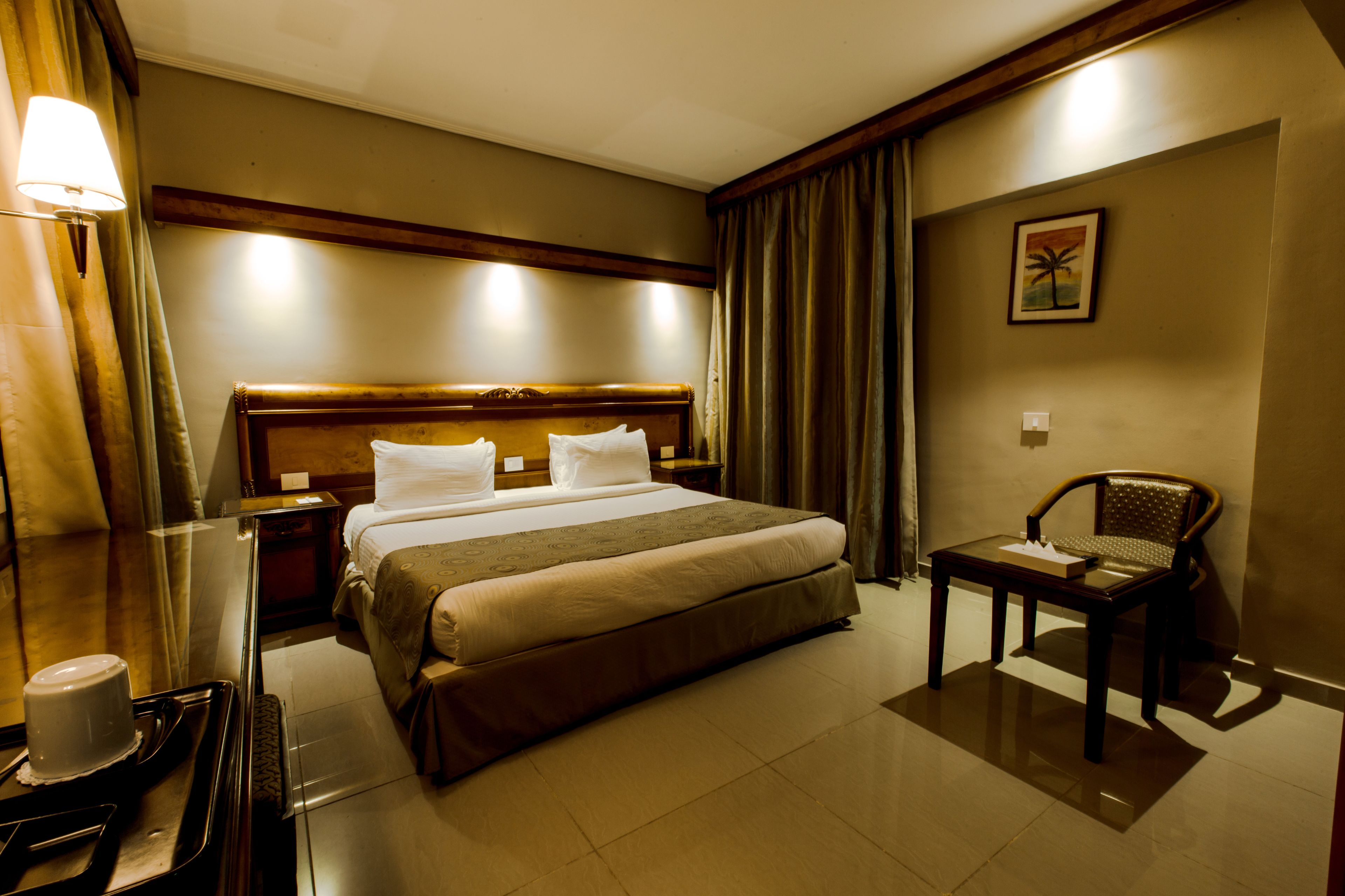 A hotel room with a large bed, a bedside table, a chair, and a mirror.
