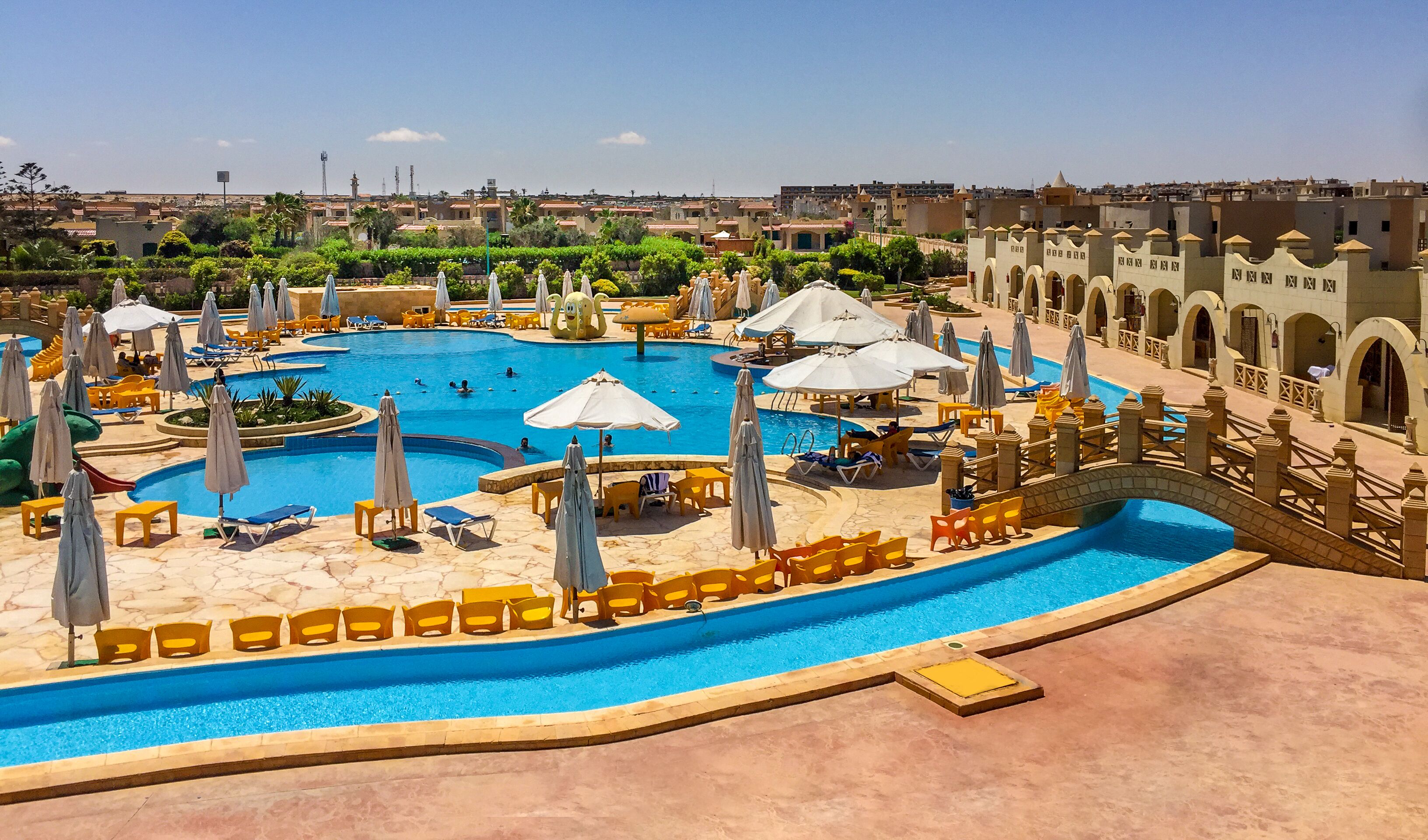 Una amplia piscina con varias pistas, rodeada de tumbonas y sombrillas.
