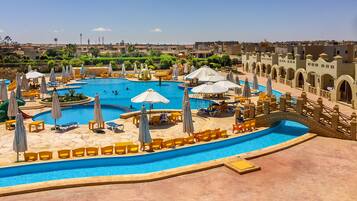 Una amplia piscina con varias pistas, rodeada de tumbonas y sombrillas.