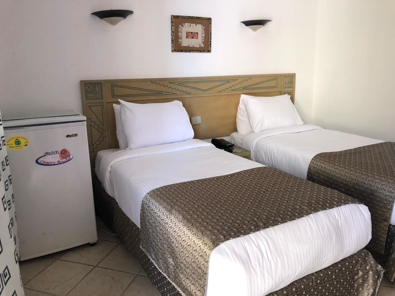 A hotel room with two beds, a refrigerator, and a wall-mounted picture.