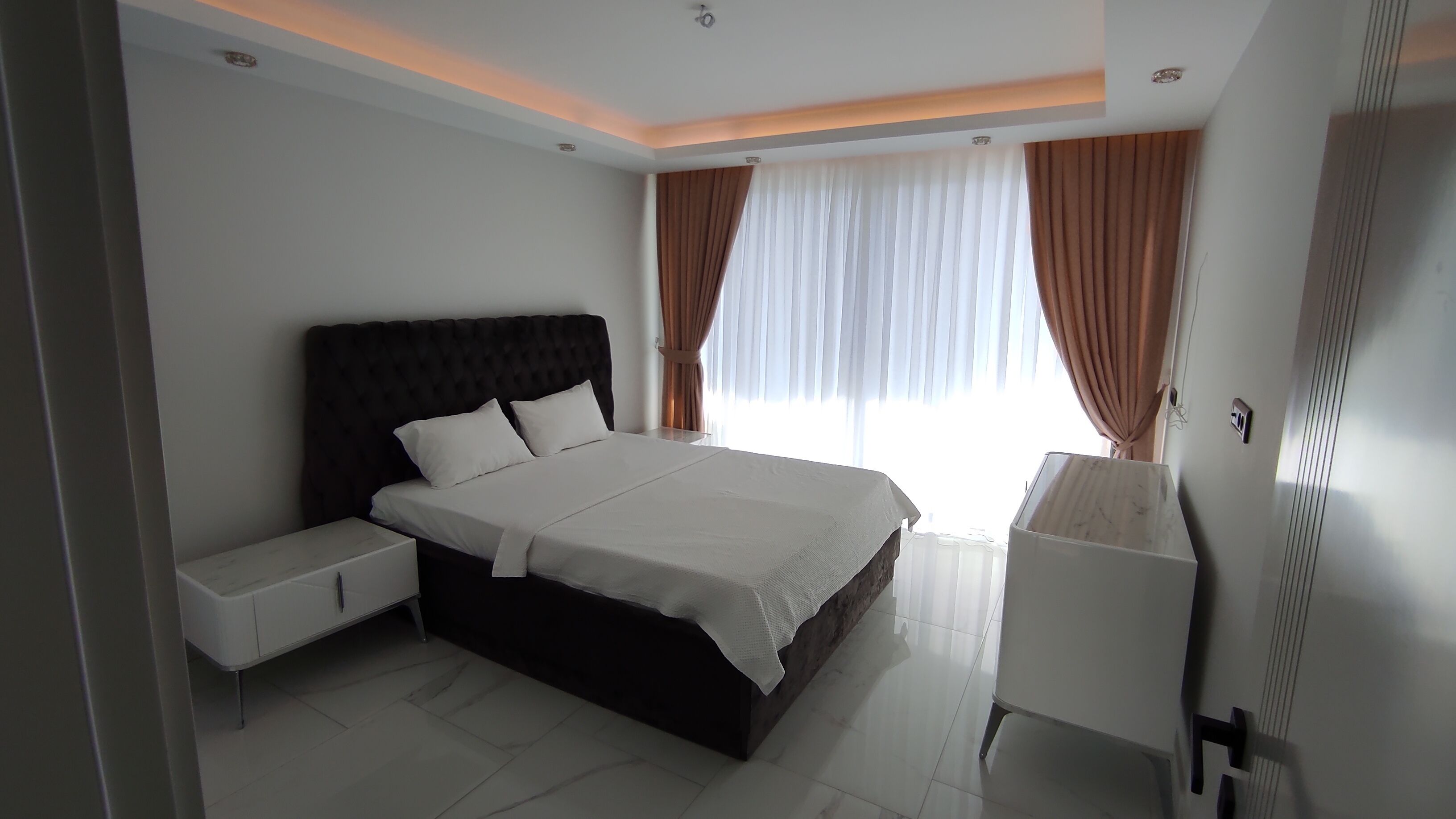 A modern bedroom with a large bed, bedside tables, and a wardrobe.