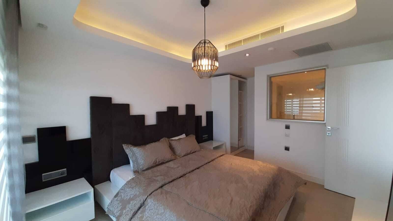 A modern bedroom with a large bed, a built-in wardrobe, and a pendant light.